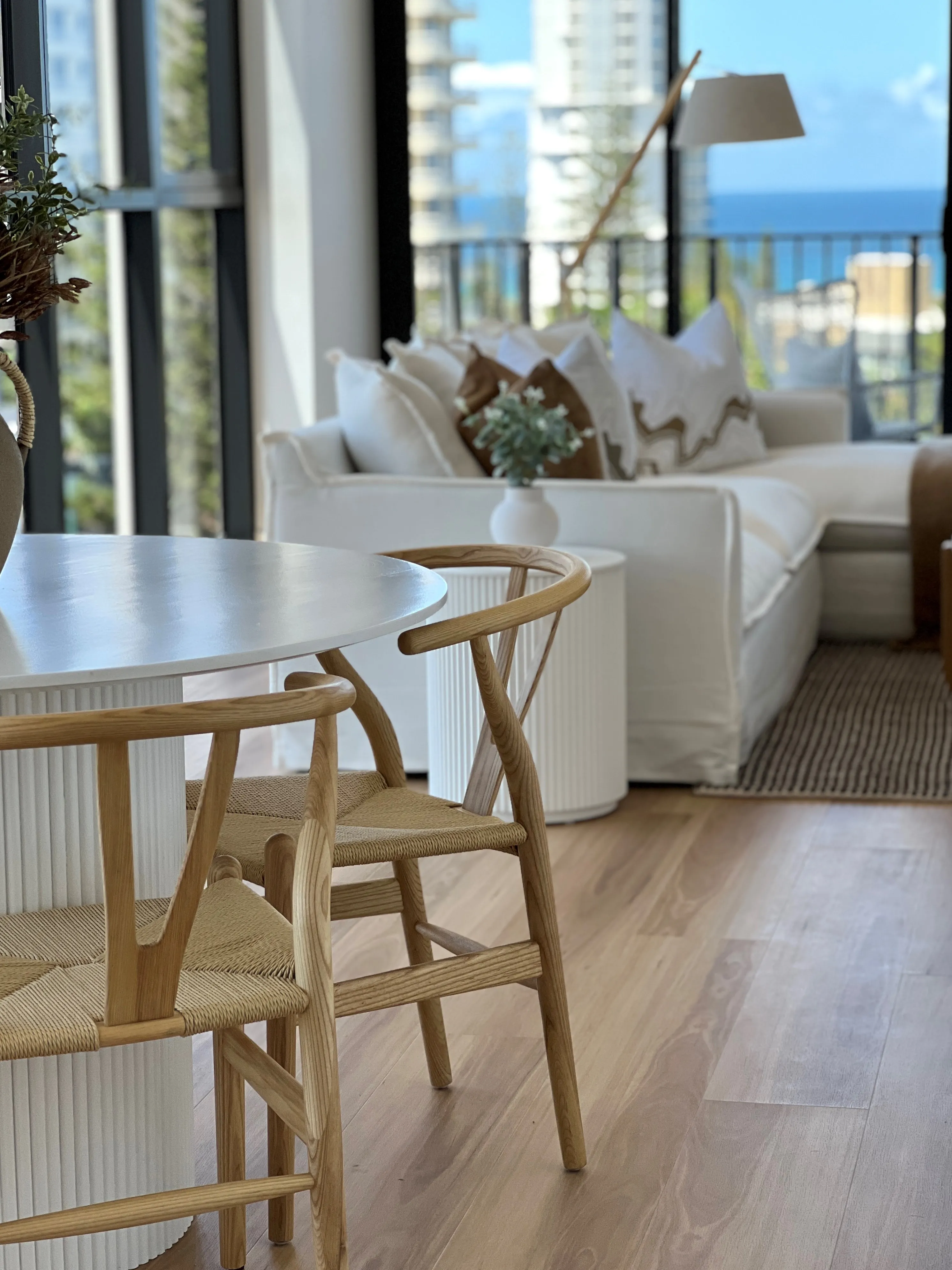Wishbone dining chairs and white fluted table with cream sofa and ocean skyline beyond